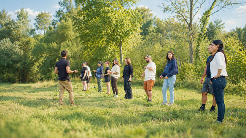 Participants utilisant des baguettes coudées pendant un atelier de radiesthésie en pleine nature.
